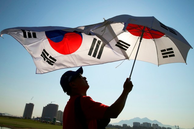 Torcedor estende bandeira sul-coreana e abre um guarda-chuva, durante a competição do golfe feminino na Rio-2016 - 17/08/2016