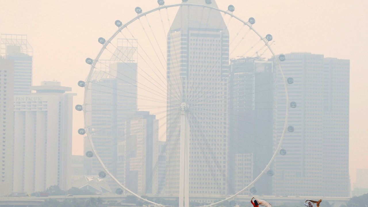 Turistas fotografam a roda-gigante 'Singapore Flyer', coberta por névoa, em Cingapura - 26/08/2016