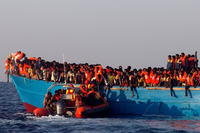Um barco de resgate da organização espanhola Proactiva se aproxima de uma embarcação de madeira superlotada com imigrantes da Eritreia, ao largo da costa da Líbia no mar Mediterrâneo - 29/08/2016