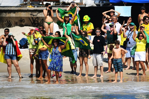 Torcedores levantam bandeiras e fotografam a prova de maratona aquática feminina, na beira da praia de Copacabana, Rio de Janeiro