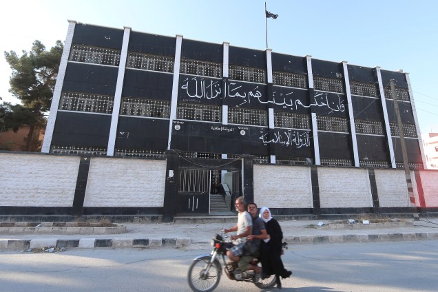 Civis passam em frente a um edifício usado como tribunal pelo Estado Islâmico na cidade retomada de Manbij, na Síria - 17/08/2016