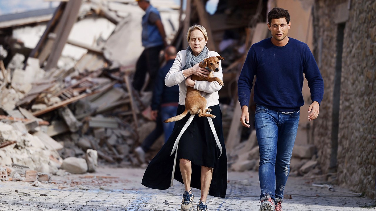 Mulher carrega cão nos braços em meio aos prédios destruídos na cidade italiana de Amatrice, após forte terremoto atingir a região - 24/08/2016