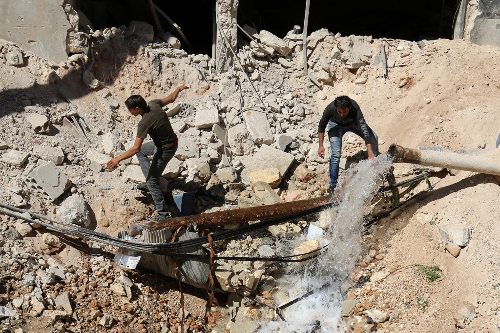 Homens inspecionam buraco no chão, resultado de um ataque aéreo na região de Aleppo, na Síria