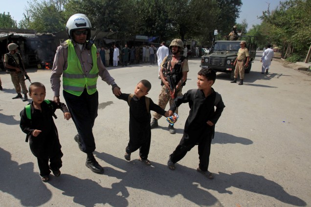 Guarda de trânsito ajuda a crianças a atravessar uma estrada enquanto o exército realiza operação após um ataque suicida em um bairro cristão nos arredores de Peshawar, no Paquistão - 02/09/2016