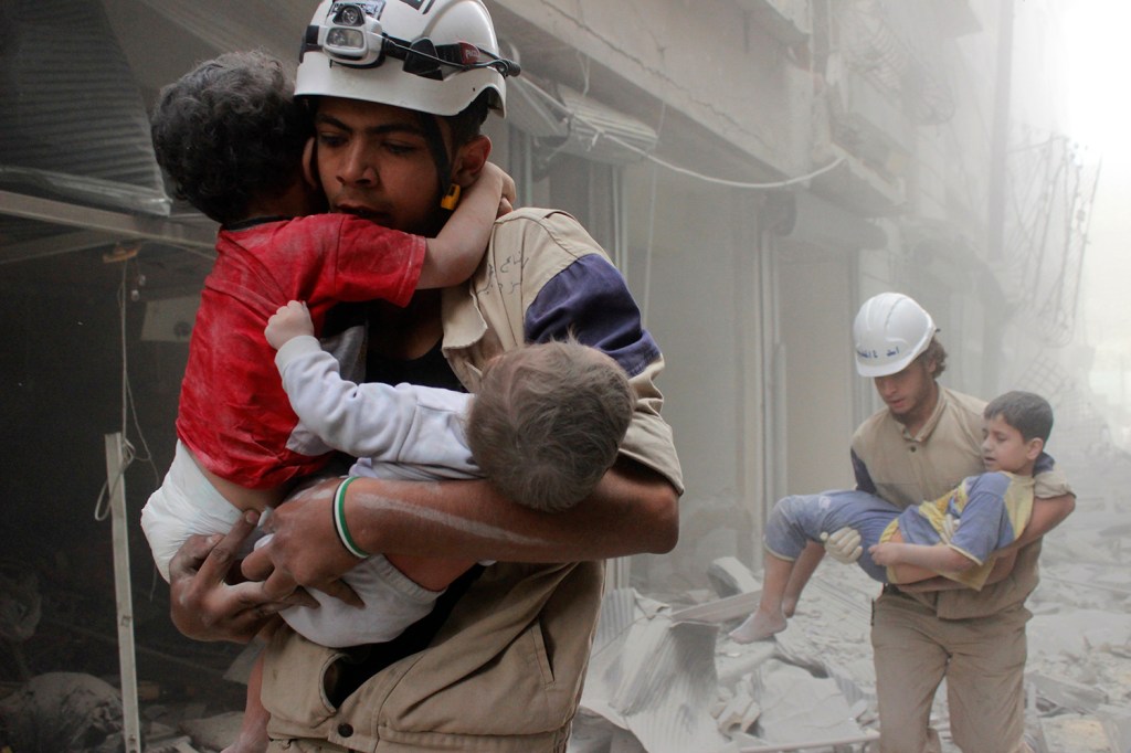 Membros da defesa civil resgatam crianças vítimas de um ataque aéreo que atingiu região vizinha a Aleppo, na Síria