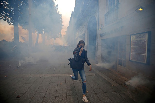Mulher corre cobrindo o rosto para se proteger das bombas de gás lacrimogêneo disparadas pela polícia francesa durante protesto contra reforma nas leis trabalhistas, em Nantes, na França - 15/09/2016