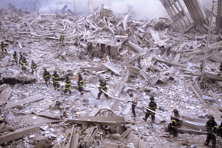Bombeiros carregam mangueira entre as ruínas do World Trade Center, na Ilha de Manhattan, em Nova York.. Na manhã do dia 11 de setembro de 2001, dois aviões comerciais foram sequestrados no Aeroporto de Boston por terroristas da Al-Qaeda, e instantes depois atingiram intencionalmente as duas torres do maior complexo comercial do planeta