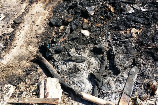 Restos do que sobrou da fogueira que foi acesa no pátio para queimar uma pilha de corpos; a foto mostra pedaços de ossos entre as cinzas