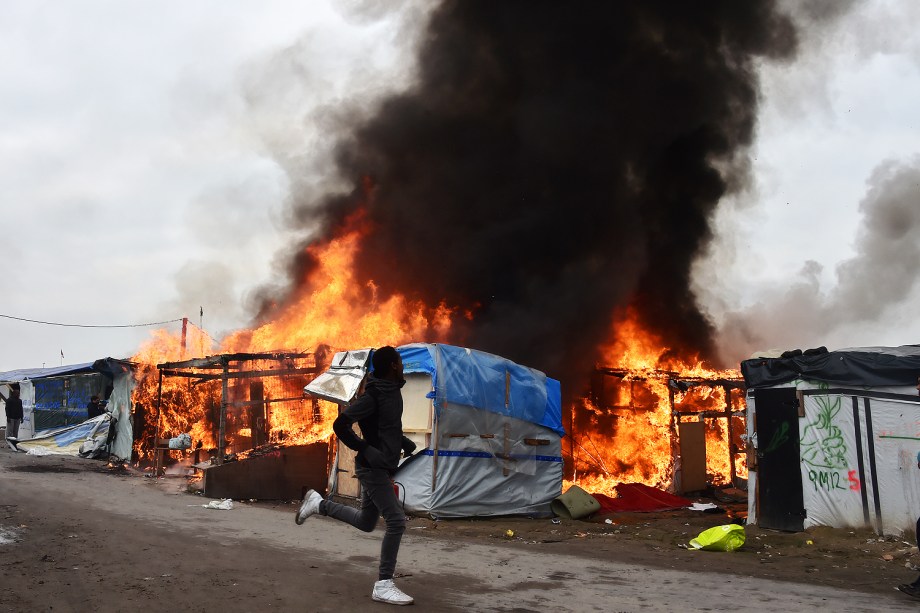 Migrante corre próximo a barracas incendidas no campo de Calais, na França - 26/10/2016
