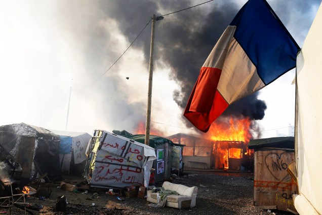 Bandeira francesa é vista no campo de Calais, na França, em meio ao incêndio provocado no local durante o terceiro dia de evacuação de refugiados - 26/10/2016