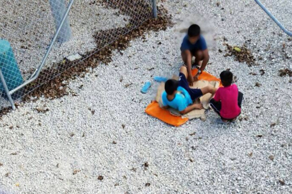 Crianças brincam perto das grades de um centro para refugiados na Austrália