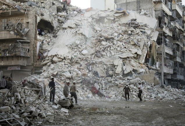 Membros da Defesa Civil da Síria, conhecidos como os Capacetes Brancos, procuram vítimas entre os escombros de um edifício destruídos após ataques aéreos no bairro Qatarji, controlado pelos rebeldes do norte da cidade de Aleppo - 17/10/2016