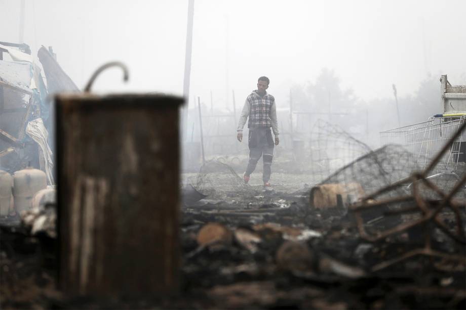 Migrante caminha entre barracas incendiadas no campo de Calais, na França. Evacuação do local já dura três dias. Os refugiados serão levados para centros de acolhimento - 26/10/2016