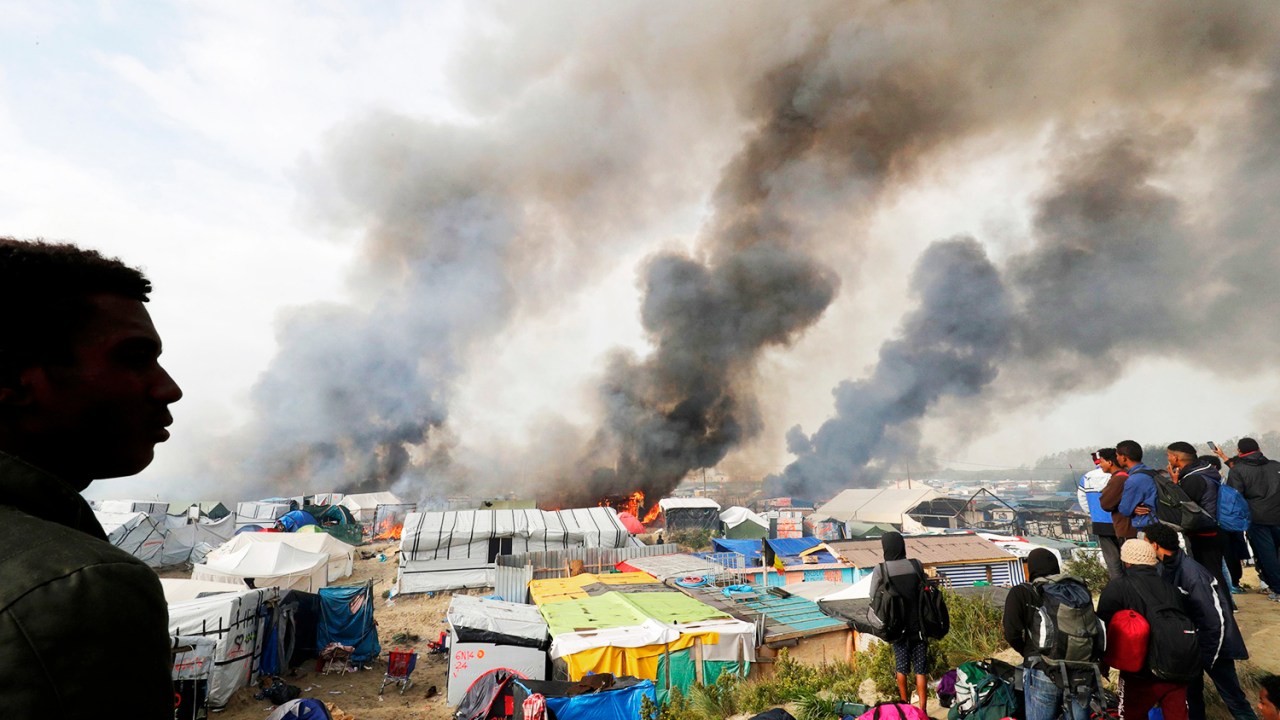 Migrantes observam barracas sendo incendiadas no campo de Calais, na França. Os refugiados serão evacuados e transferidos para centros de acolhimento - 26/10/2016