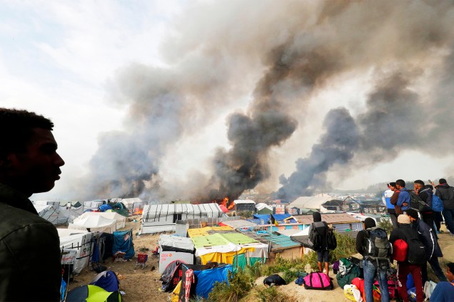 Migrantes observam barracas sendo incendiadas no campo de Calais, na França. Os refugiados serão evacuados e transferidos para centros de acolhimento - 26/10/2016
