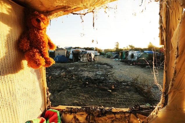 A teddy bear left behind my migrants hangs at the demolished "Jungle" migrant camp in Calais in northern France on October 28, 2016. Migrants left behind after the demolition of France's notorious "Jungle" faced a day of reckoning after spending the night, with official blessing, in a disused part of the camp. After thousands were bussed out over the past two days, the camp next to the northern port of Calais was virtually deserted. But scores of lost souls were still looking for shelter -- or refusing to leave the squalid settlement that has become one of the most visible symbols of Europe's migrant crisis. / AFP PHOTO / FranÁois NASCIMBENI
