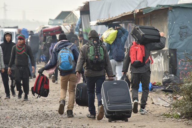 Imigrantes caminham com suas malas em direção a um ponto de encontro definido pelas autoridades francesas como parte da evacuação completa do campo de Calais - 24/10/2016