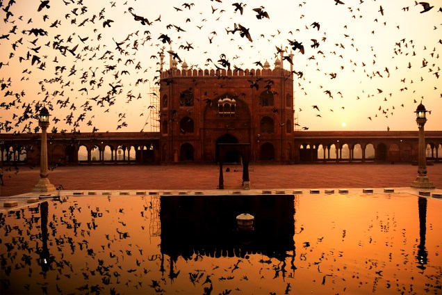 Pássaros voam sobre a mesquita de Jama Masjid, durante pôr do sol em Nova Déli, na Índia - 27/10/2016