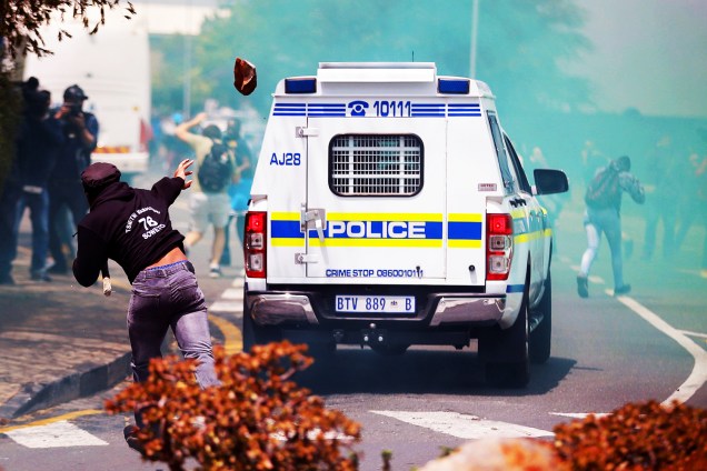 Estudante arremessa pedra em carro policial sul-africano, em protesto contra altas taxas de matrícula na Universidade de Joanesburgo, na região de Witwatersrand - 04/10/2016