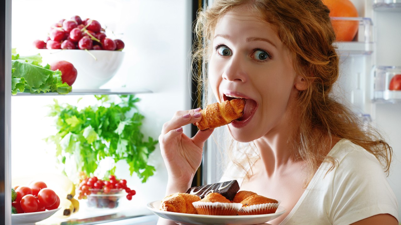 Mulher comendo na frente da geladeira