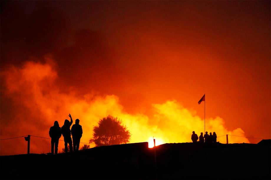 Migrantes são vistos próximos a chamas, durante o segundo dia de evacuação do acampamento localizado em Calais, na França - 25/10/2016