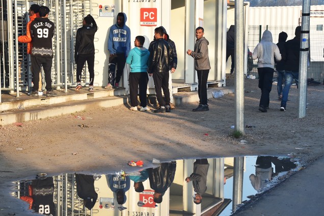 Reflexo de migrantes é visto em uma poça d'água, durante evacuação do acampamento de refugiados localizado em Calais, na França - 25/10/2016