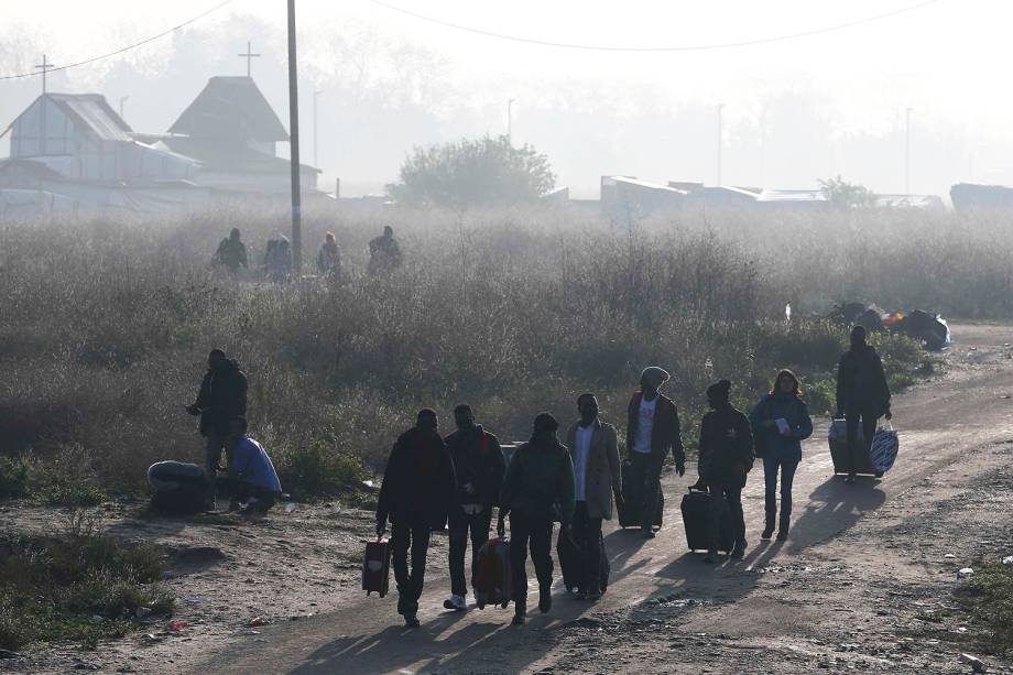 Migrantes carregam seus pertences durante evacuação do acampamento improvisado de refugiados, localizado em Calais, na França - 25/10/2016