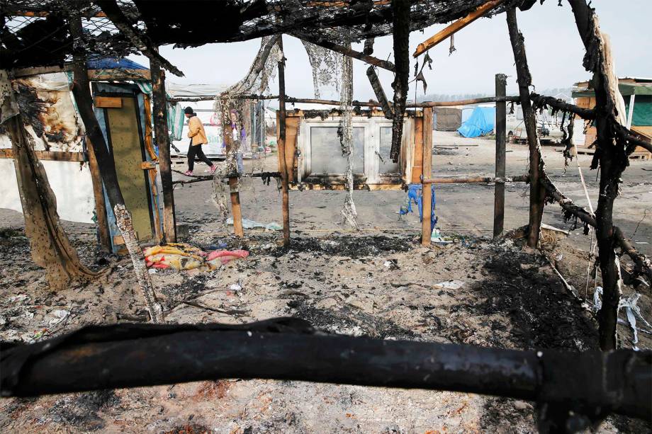 Migrante caminha próxima a barracas incendiadas no campo de Calais, na França, durante o terceiro dia de evacuação do local - 26/10/2016