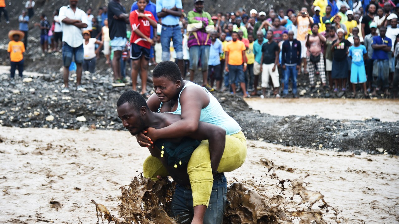 Homem carrega mulher ao atravessar rio durante a passagem do furacão Matthew no Haiti - 05/10/2016