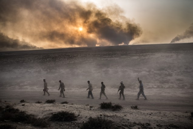 Soldados iraquianos caminham em uma estrada enquanto uma coluna de fumaça é vista ao fundo, em Qayyarah, ao sul de Mosul - 19/10/2016