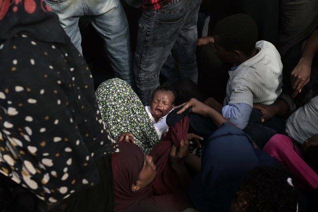 Criança chora no colo de sua mãe enquanto dezenas de imigrantes e refugiados aguardam pelo resgate em um barco à deriva no Mar Mediterrâneo