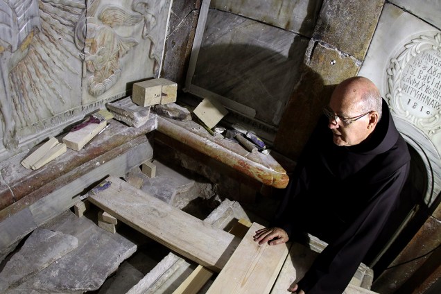 Frei Franciscano observa o local em que Jesus Cristo teria sido sepultado, segundo a tradição cristã. Após a remoção das placas de mármore, foi possível encontrar, intacta, a cama funerária onde acredita-se que o corpo teria sido colocado.