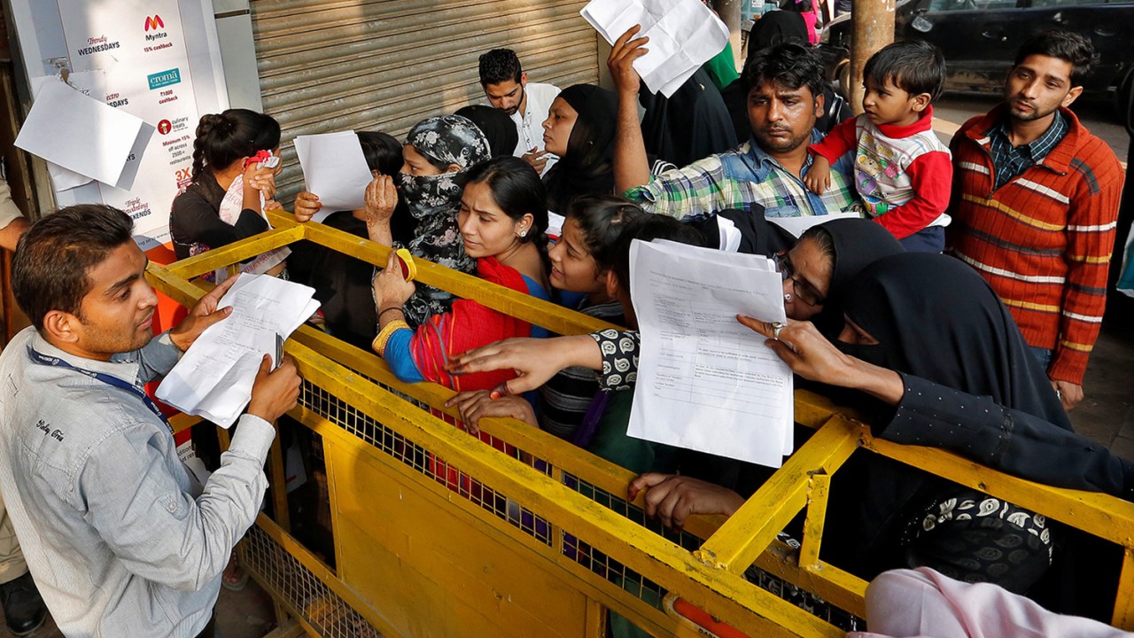 Funcionário de banco indiano distribui requerimentos para troca de notas que serão retiradas de circulação, na Índia