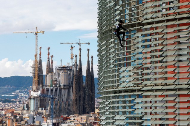 O alpinista francês Alain Robert, também conhecido como "O Homem Aranha Francês" escala um a Torre Agbar de 38 andares com a catedral da Sagrada Família ao fundo em Barcelona, na Espanha - 25/11/2016