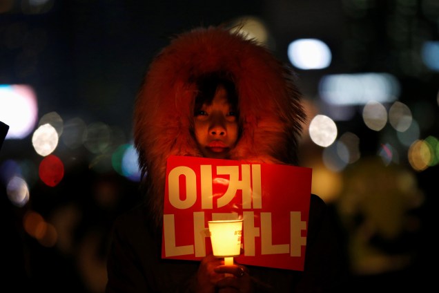 Manifestante segura uma vela e um cartaz durante protesto que pede a saída da presidente Geun-hye em Seul, na Coreia do Sul - 25/11/2016