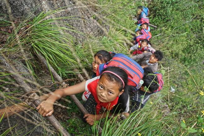 Os alunos do vilarejo de Atuler sobem um penhasco para voltar da escola pra casa na região autônoma de Liangshan Yi, província de Sichuan, na China