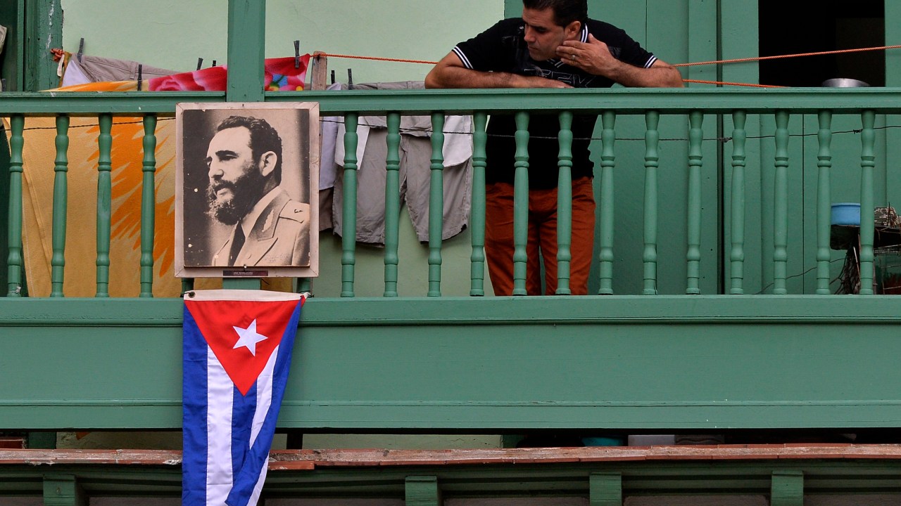 Homem exibe retrato do líder revolucionário Fidel Castro e a bandeira cubana, em uma sacada da cidade de San Francisco de Asis, em Havana - 27/11/2016