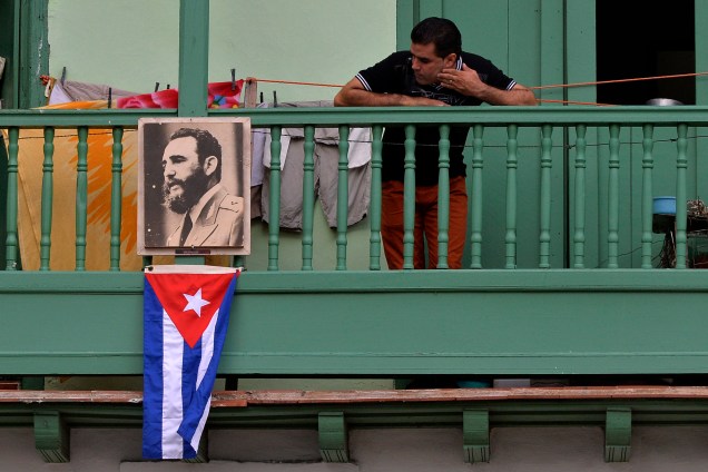 Homem exibe retrato do líder revolucionário Fidel Castro e a bandeira cubana, em uma sacada da cidade de San Francisco de Asis, em Havana - 27/11/2016