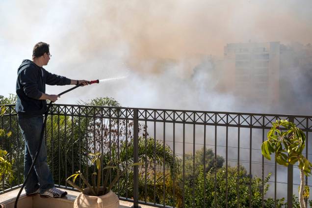 Homem usa uma mangueira para tentar apagar o fogo de um telhado na cidade portuária de Haifa, norte de Israel - 24/11/2016 Homem usa uma mangueira para tentar apagar o fogo de um telhado na cidade portuária de Haifa, norte de Israel - 24/11/2016