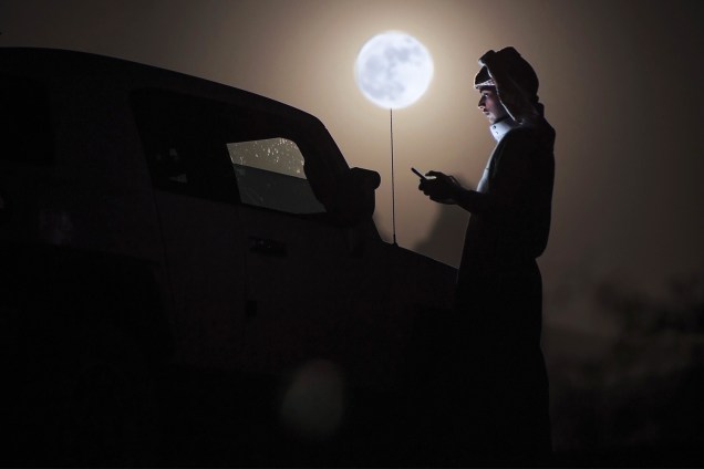 Homem observa celular durante a passagem do fenômeno 'Superlua', em Tabuk, na Arábia Saudita - 14/11/2016