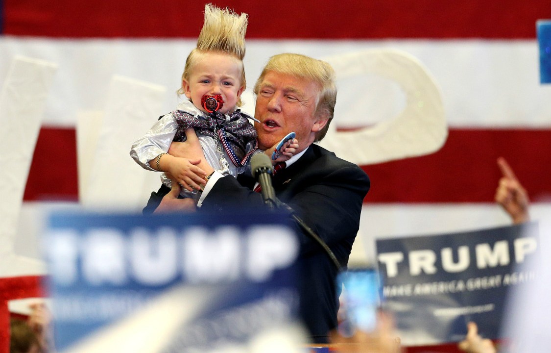 Donald Trump segura uma criança 'topetuda' em su último evento, em New Hampshire