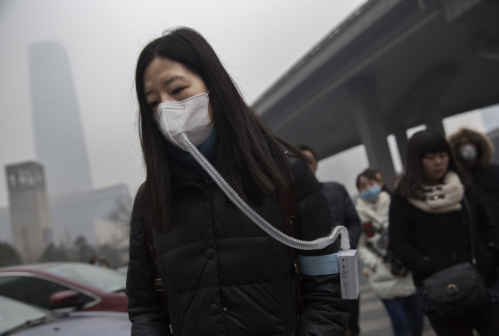 Mulher com máscara contra poluição em Pequim, na China. A cidade decretou alerta vermelho no início de dezembro, pela primeira vez. Crédito Kevin Frayer/Getty Images