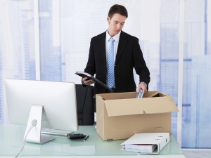 Businessman Collecting Office Supply In Cardboard Box At Desk