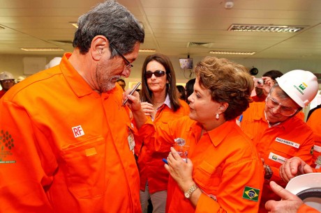 Dilma Rousseff autografa o macacão do ex-presidente da Petrobras, José Sérgio Gabrielli. Ao fundo, é observada por Graça Foster, também investigada pela compra de Pasadena e Paulo Roberto Costa, delator do esquema de corrupção na estatal