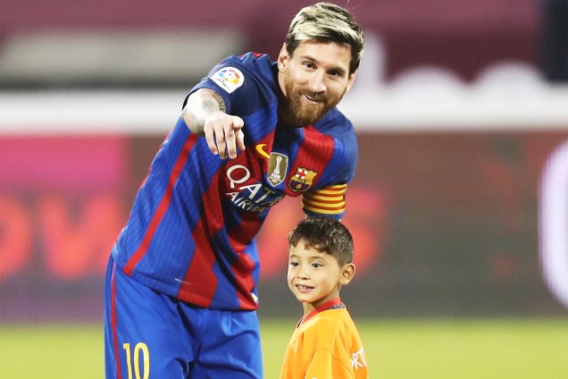 O jogador do Barcelona, Lionel Messi, entra em campo com o garoto afegão Murtaza Ahmadi, em partida amistosa contra o Al-Ahli, em Doha, no Catar - 13/12/2016