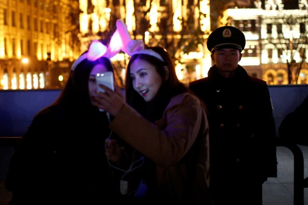 Mulheres tiram uma selfie ao lado de um oficial de polícia enquanto participam nas celebrações de Ano Novo, em Xangai na China