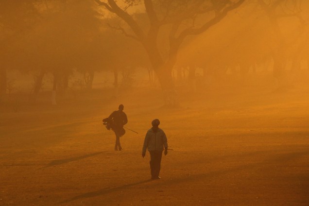 Jogador de golfe e seu ajudante caminham por um campo em uma manhã enevoada de inverno na Índia - 30/12/2016