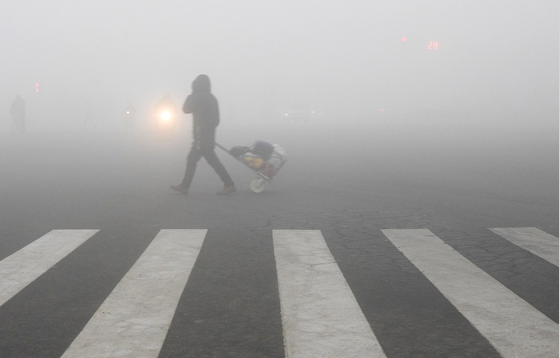 Pedestre caminha com carrinho de compras em rua na cidade de Luanyungang, na China, sob espessa fumaça tóxica de poluição