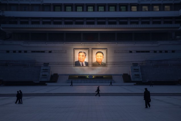 Pedestres caminham por uma praça onde estão pendurados dois retratos: do atual presidente King Jon Il (dir.) e do ex-presidente, falecido Kim Il-Sung, em Pyongyang - 01/12/2016