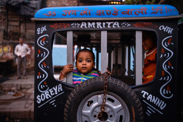 Criança indiana olha por detrás de uma carroça durante festival em Nova Délhi, na Índia - 01/12/2016